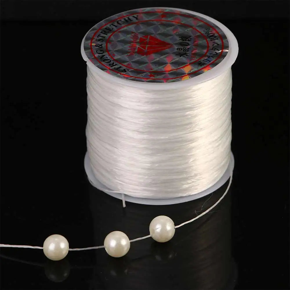 Spool of white stretchy crystal beading cord with pearls unwound on a black surface