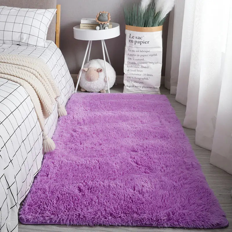 A fluffy purple Nordic fur rug placed on a light wooden floor next to a white storage stand and a potted plant.