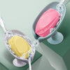 Two pink and yellow leaf-shaped suction cup soaps are draining in a silver dish.
