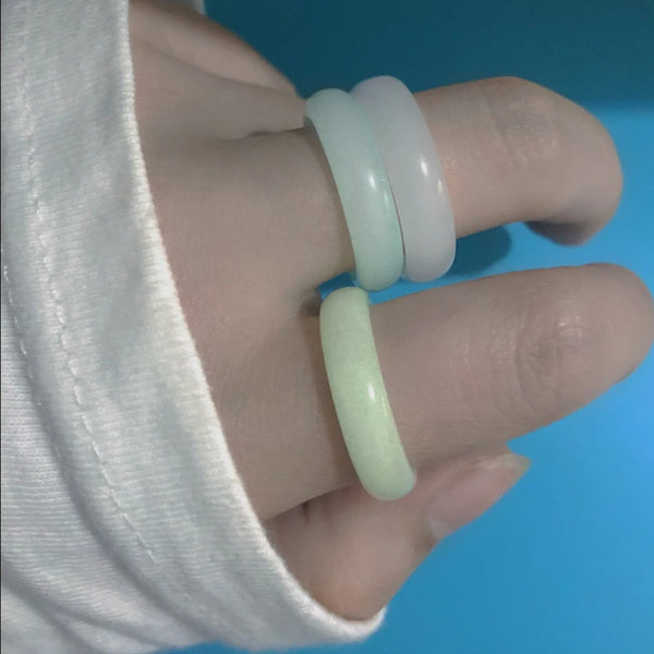 Una mano vistiendo una pila de anillos de piedra luminosos en verde claro y blanco en el dedo.