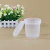 A clear plastic storage bucket with a tamper-evident lid next to a white planter of pink and white flowers.