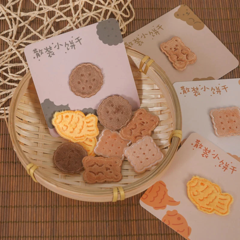 A collection of food-themed iron-on patches, including cookies and fish shapes, are displayed in a woven basket.