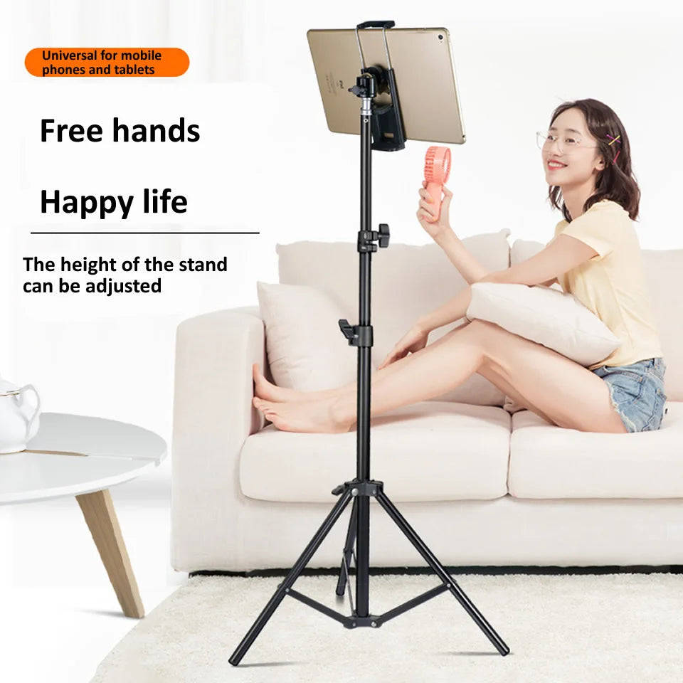 A woman is using an adjustable aluminum tripod stand to hold a tablet or phone while relaxing on a sofa.