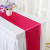 A pink satin table runner is draped on a white tablecloth with a small bouquet of purple and yellow flowers.