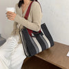 A woman holds a beige knit sweater and a white cup while resting beside a black and white striped canvas crossbody tote bag.