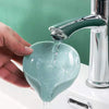 A hand pours water into a leaf-shaped suction cup soap dish with a self-draining tray.
