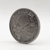 A round, silver-toned commemorative coin featuring a stylized skull and crossbones design.