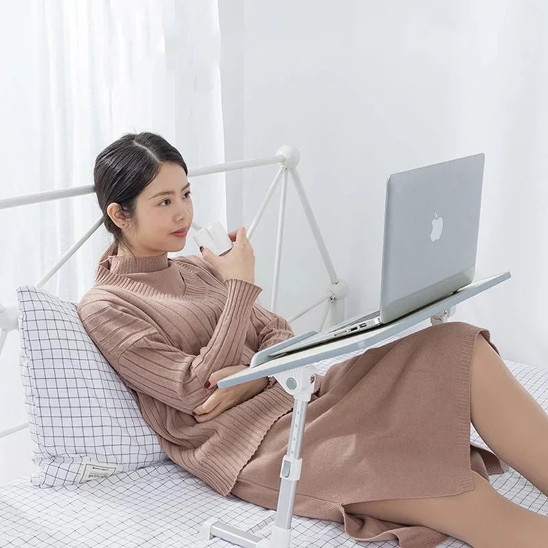 A woman is using an adjustable foldable laptop desk on a bed to work on a laptop.