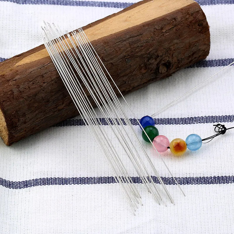 A bundle of stainless steel beading needles is laid across a wooden cylinder on a white cloth.