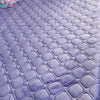 A purple quilted velvet bedspread with a diamond pattern laid out on a floor.