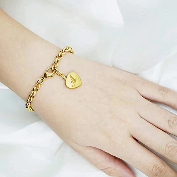 Bracelet charm alphabet cœur doré porté au poignet sur fond blanc.