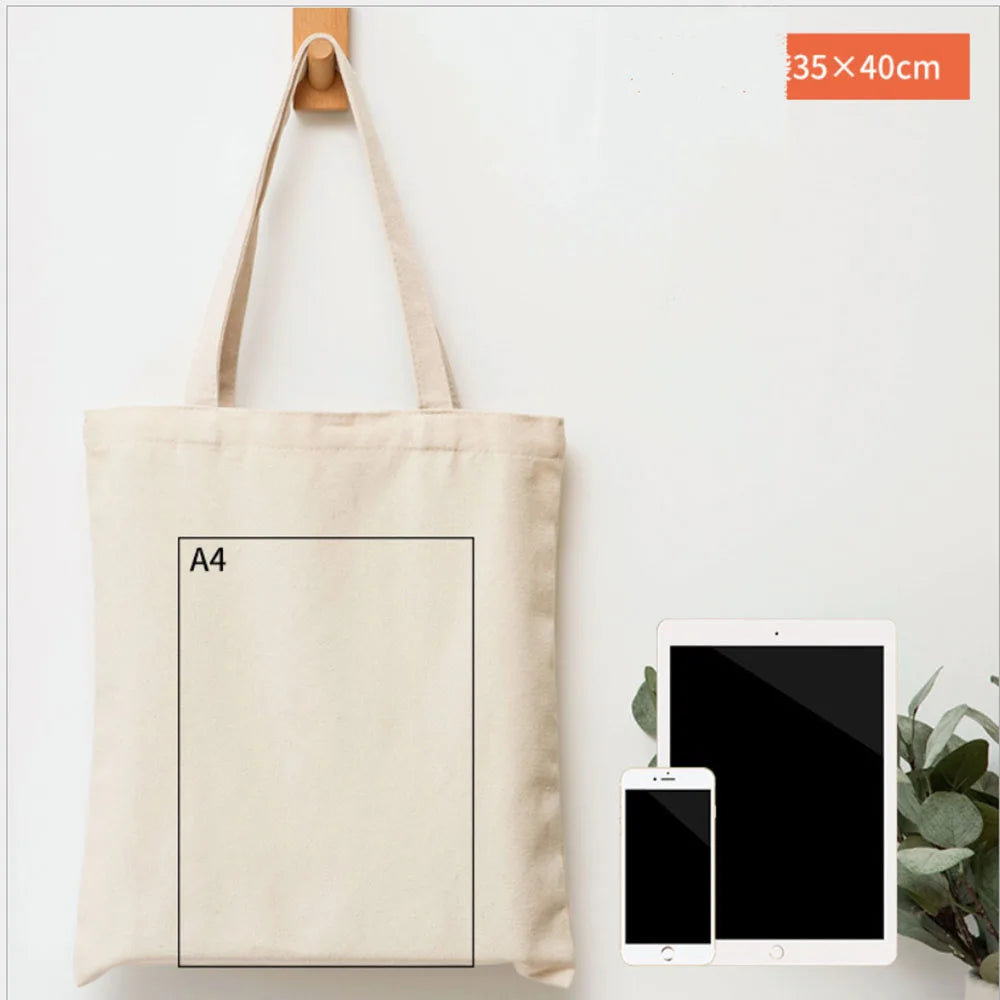 A beige canvas tote bag with an A4 sized rectangular insert, shown next to a tablet and a plant.