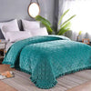 Teal quilted velvet bedspread with a diamond pattern draped over a bed.