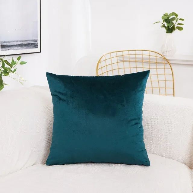 A dark teal velvet decorative cushion cover resting on a white sofa.