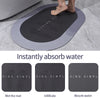 A black bath mat is shown being used to absorb water on a gray tiled floor.