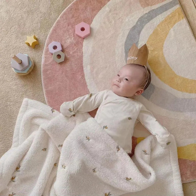 A baby is lying on a pink and cream patterned blanket, wrapped in a white coral fleece blanket.