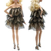 A fashion doll wearing a black and gold tiered ruffle dress with sheer mesh detailing.