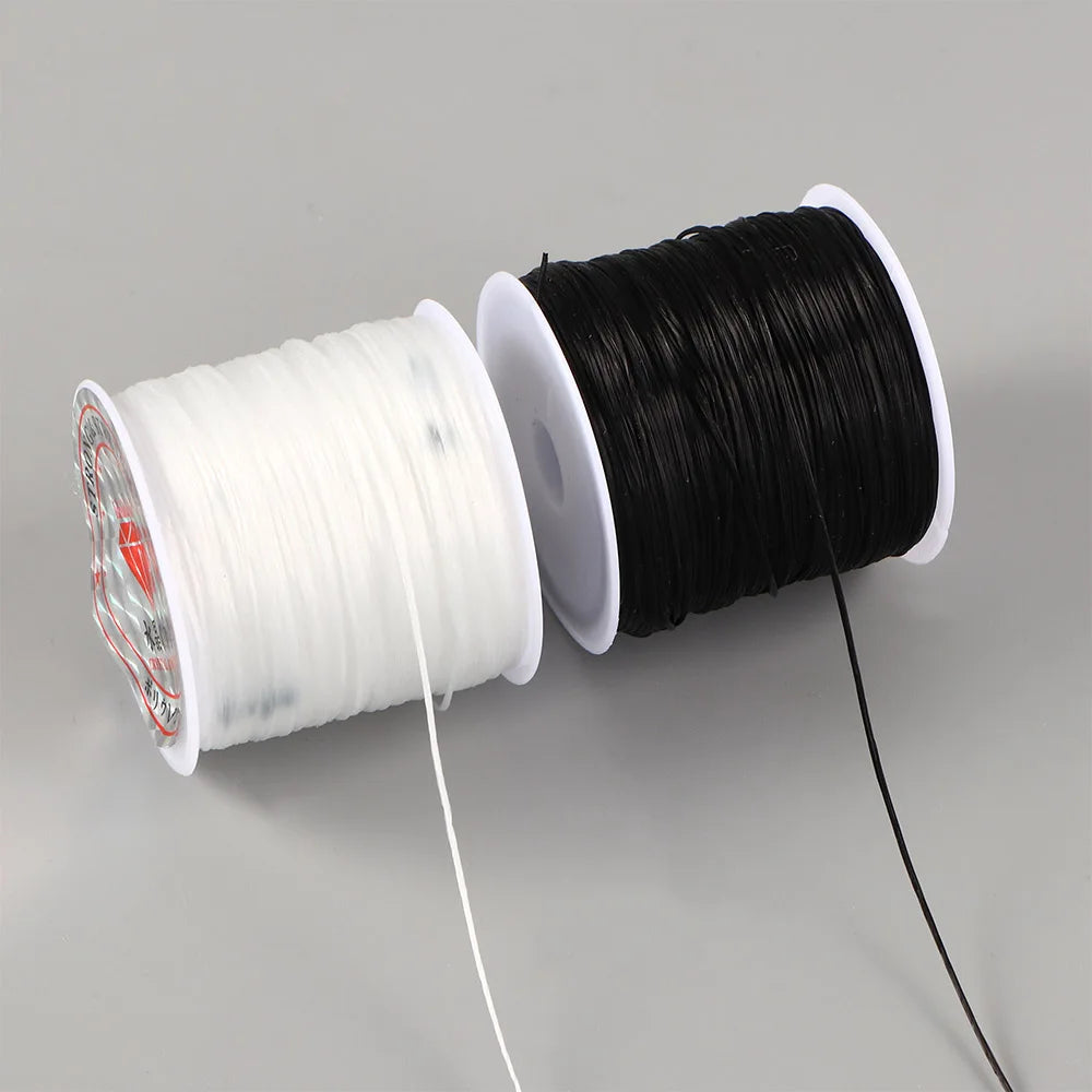 A spool of black elastic crystal beading cord next to a spool of white elastic crystal beading cord.