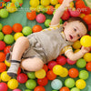 A baby is surrounded by a large assortment of colorful, soft play balls in shades of yellow, orange, and green.