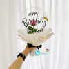 A hand holds a clear balloon featuring the text Happy Birthday Moon with a gold crown and green leaf.