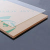 A clear acrylic sheet is placed on a light brown wooden board, showing the text CAST ACRYL and a green design.