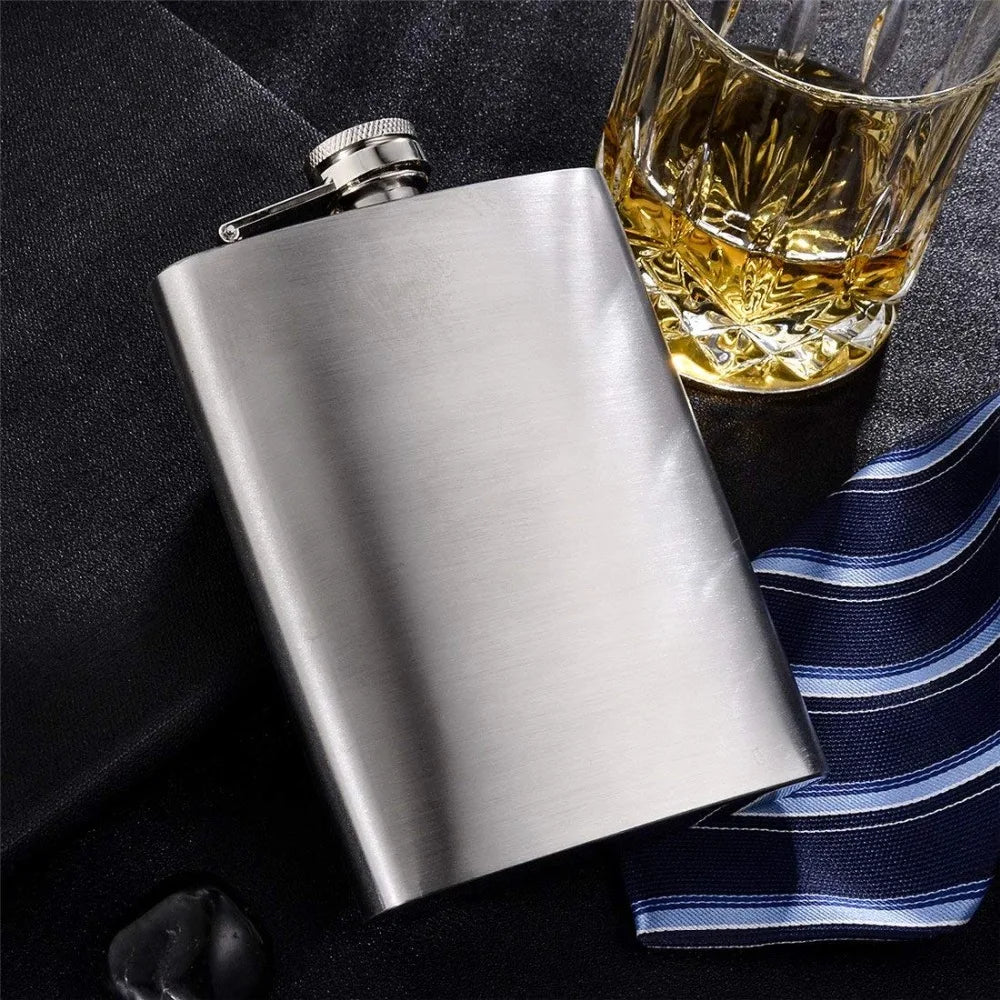 Silberne Edelstahlflasche mit Metalltrichter neben einem Glas bernsteinfarbigem Flüssigkeit und einem gestreiften Tuch.