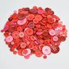 A pile of assorted eco-friendly wooden buttons in shades of pink, coral, and red.