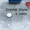Clear crystal stone pebbles ranging from 1 to 3 mm size scattered on a white surface.