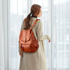 A woman wearing a tan coat carries a brown vintage faux leather backpack with multiple compartments.