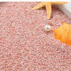 Orange starfish, seashell, and pearl resting on pink decorative stone pebbles.