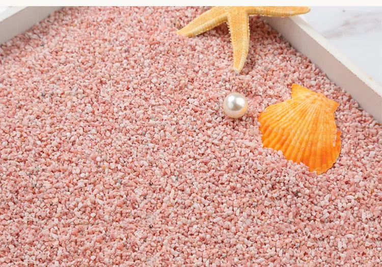 Orange starfish, seashell, and pearl resting on pink decorative stone pebbles.