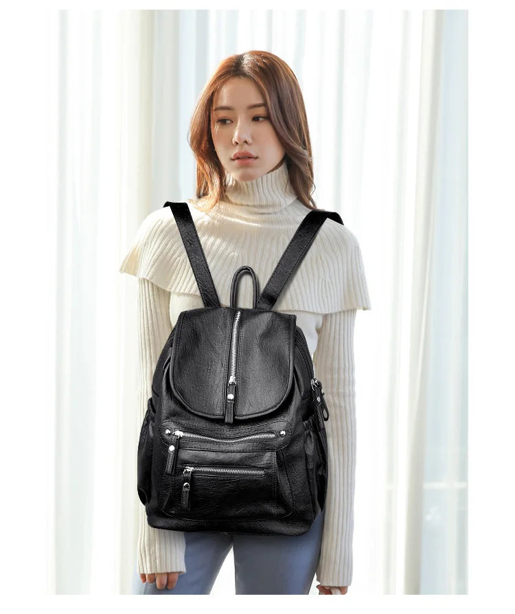 A woman wearing a black vintage faux leather backpack with multiple compartments.