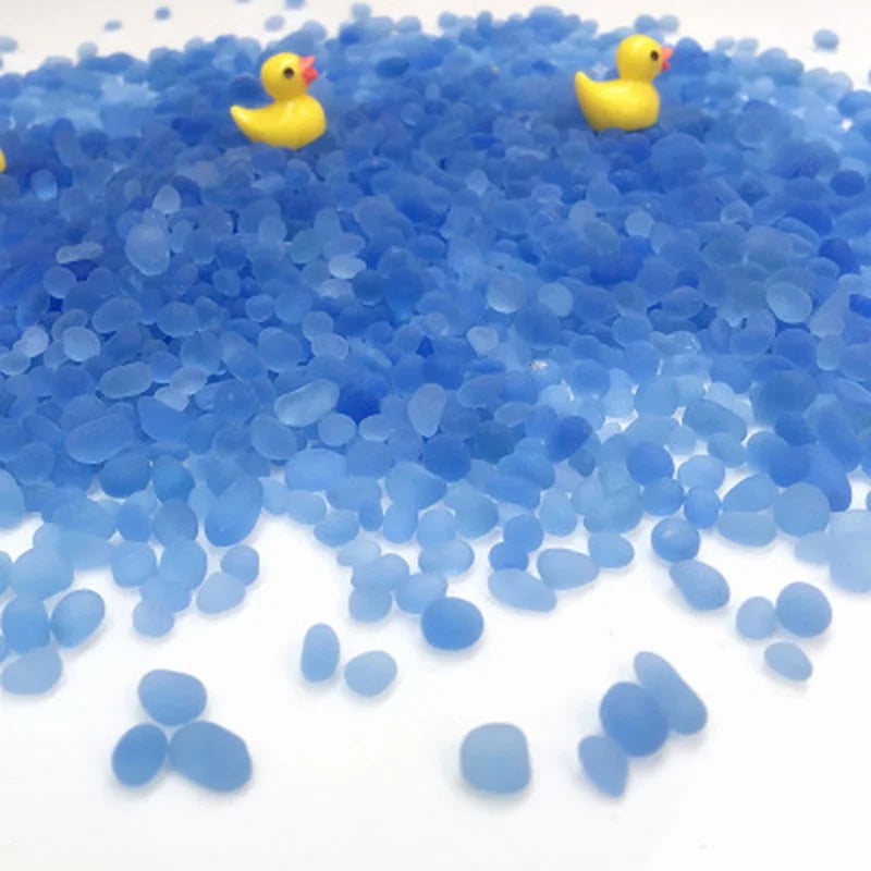 A pile of small, bright blue decorative stone pebbles with a few yellow ducks scattered on top.