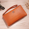A tan Litchi-Grain PU leather long wallet with a strap is shown resting on a light wooden surface.