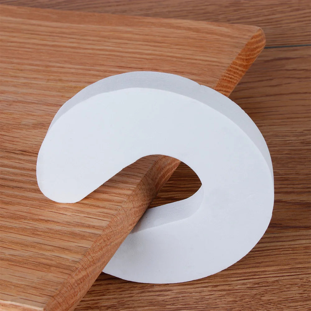 A white foam door stopper with a curved shape is shown resting on a wooden surface.
