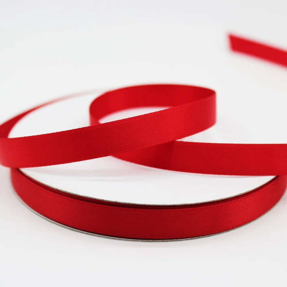 Red satin ribbon rolls coiled and overlapping on a white background.