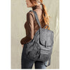 A woman wearing a brown turtleneck and dark jeans is carrying a gray vintage faux leather backpack.