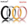 Four braided silicone rings in black, white, gold, and pink colors displayed on a reflective surface.