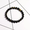 A stretch bracelet made of natural black and gold obsidian gemstones worn against a white background.