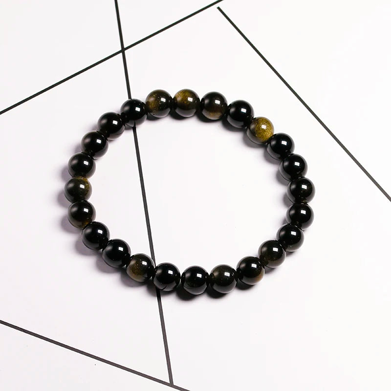 A stretch bracelet made of natural black and gold obsidian gemstones worn against a white background.