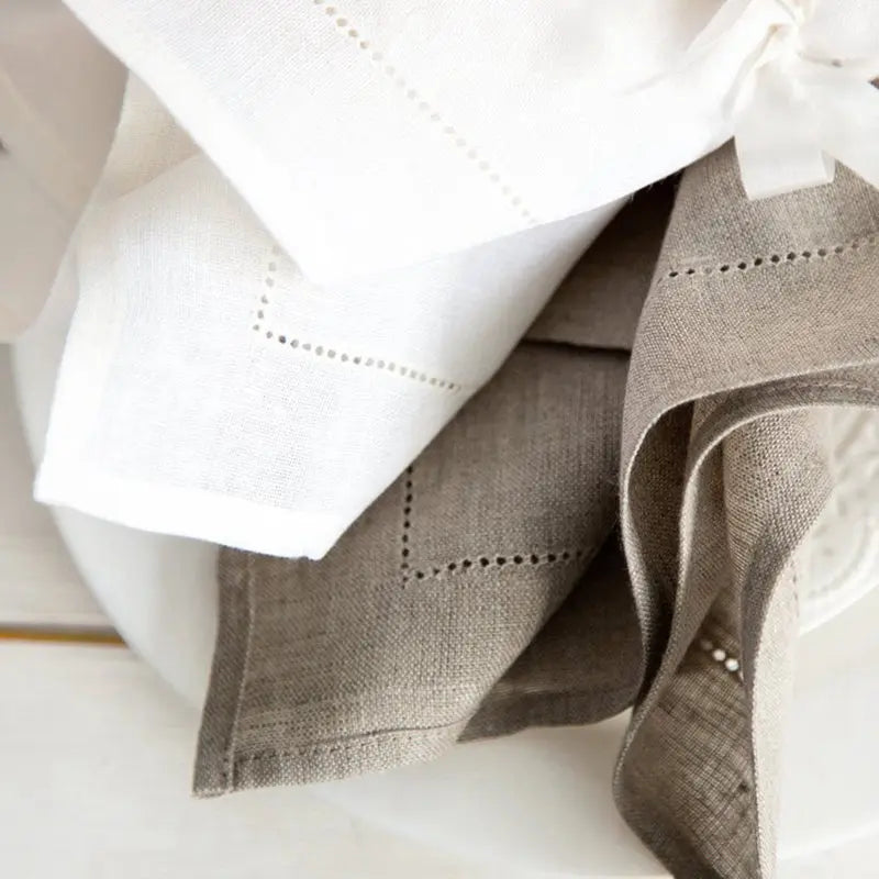 A stack of six linen hemstitch napkins in natural beige and white fabric.