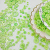 A close-up of a large assortment of light green wooden buttons scattered on a white surface.