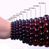 A hand is wearing a stretch bracelet made of dark red black gold obsidian gemstones.