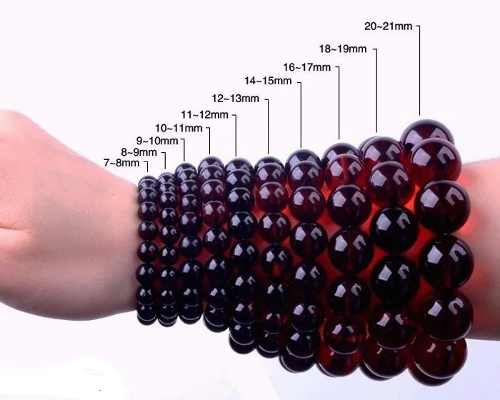 A hand is wearing a stretch bracelet made of dark red black gold obsidian gemstones.