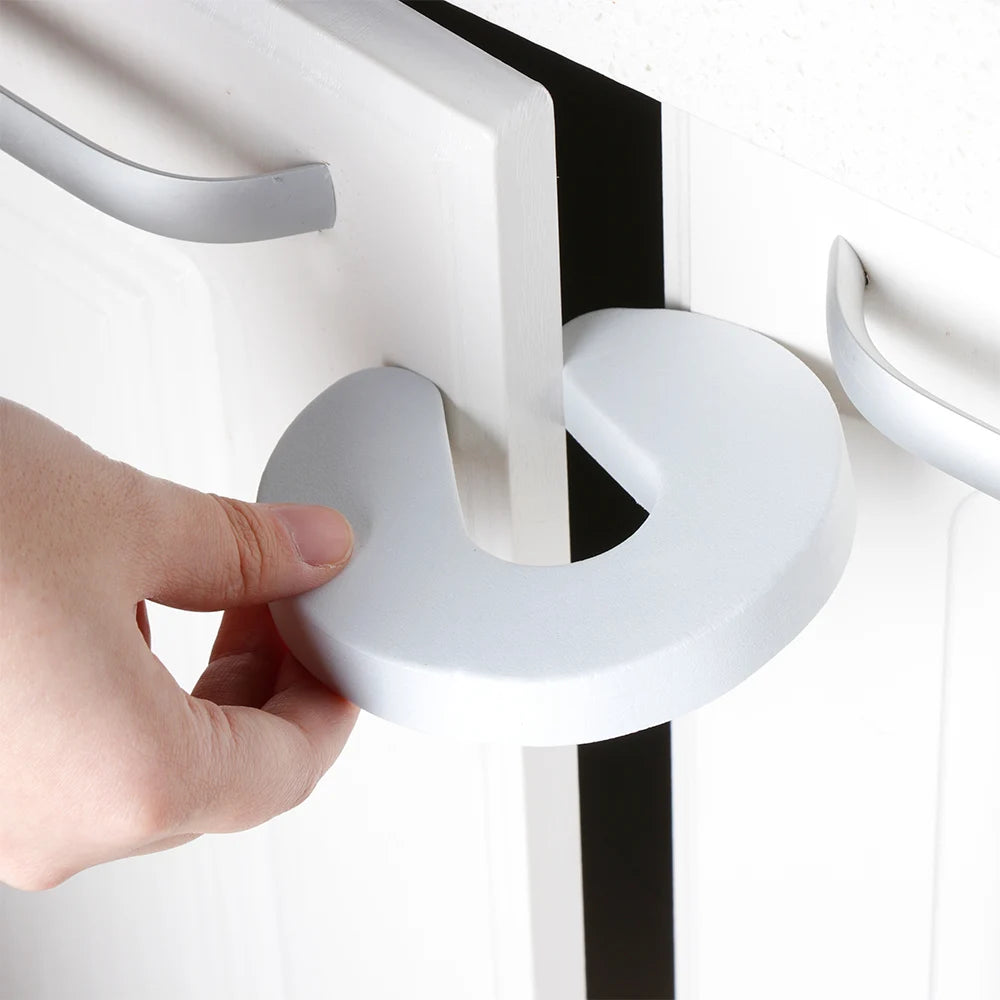 A hand is gripping a white foam door stopper with a finger pinch protection feature.