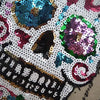 A close-up of a sequin skull embroidered patch featuring purple, teal, and pink sequins on a white background.