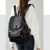 A woman is shown wearing a black vintage faux leather backpack with multiple compartments over a white sweater and dark jeans