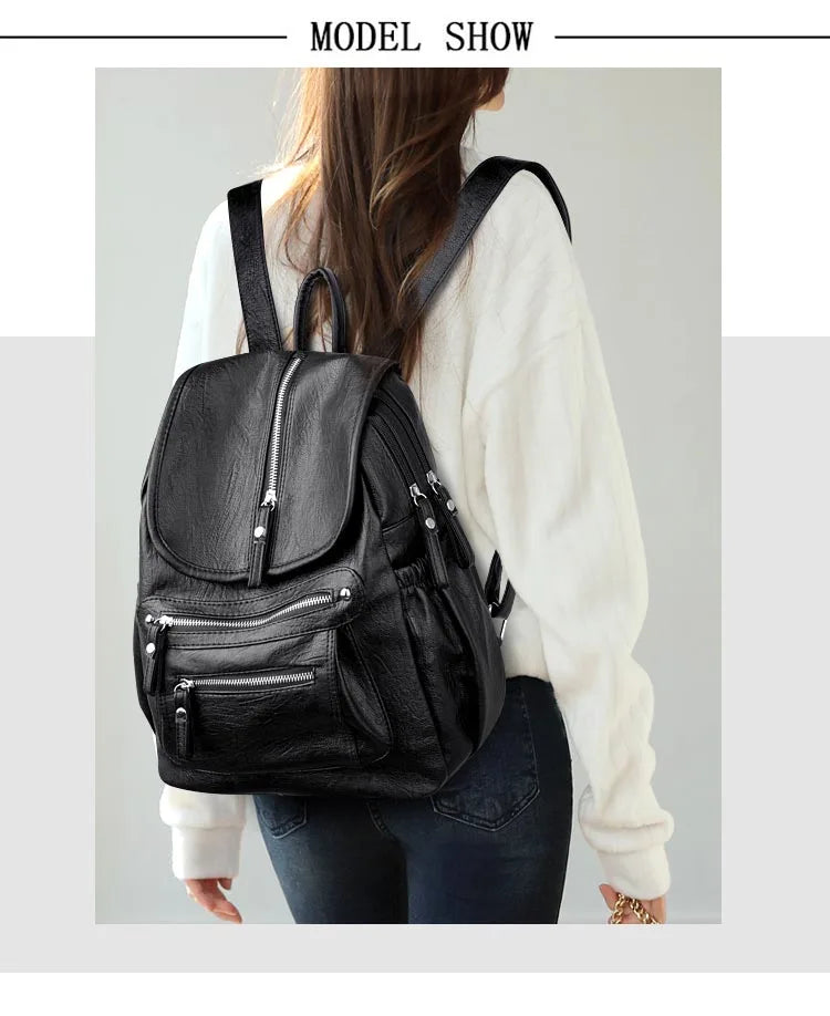 A woman is shown wearing a black vintage faux leather backpack with multiple compartments over a white sweater and dark jeans