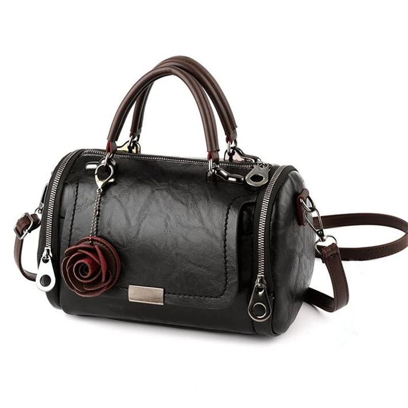 A black leather crossbody shoulder bag with brown leather handles and a rose pendant.