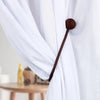 A close-up of a dark brown magnetic pearl ball curtain tieback with a rope handle against a white fabric.